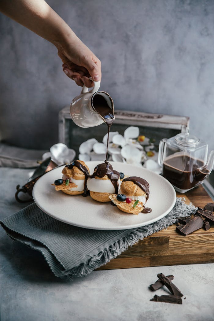 Profiteroles topped with chocolate sauce being poured. A tempting dessert perfect for sweet lovers.